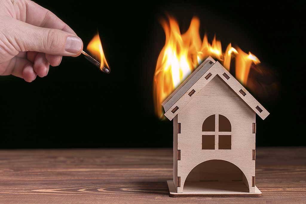 Model house in fire and hand with matchstick on a black backgrou Model house in fire and hand with matchstick on a black backgrou