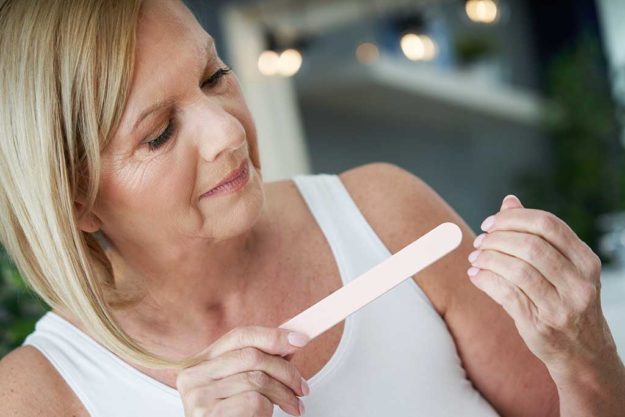 Senior woman using nail file in the bathroom Picture of senior woman using nail file in the bathroom