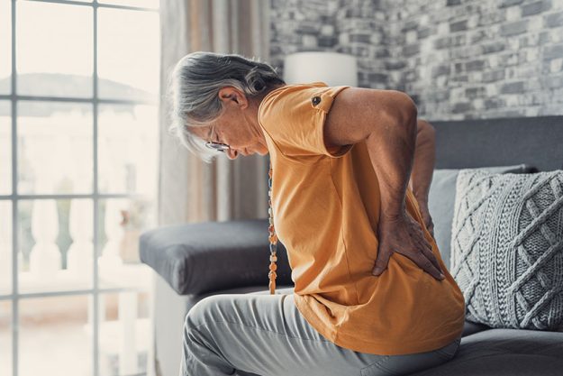 unhappy-mature-woman-touching-back-feeling-pain-sitting-couch-living Unhappy mature woman touching back, feeling pain sitting couch living