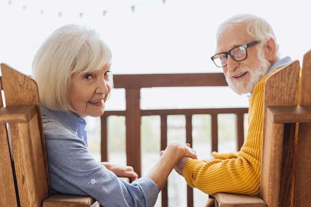 smiling elderly couple looking camera holding hands while sitting armchairs smiling elderly couple looking camera holding hands while sitting armchairs