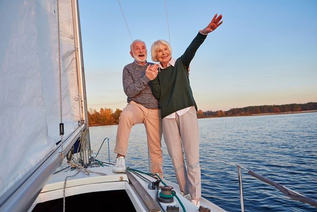 Excited senior couple holding hands and smiling while standing on the side of yacht deck Excited senior couple holding hands and smiling while standing on the side of yacht deck