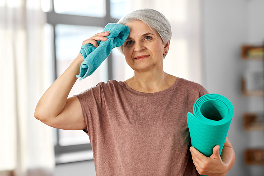 Happy tired senior woman with yoga mat and towel