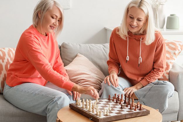 Mature female friends playing chess home Mature female friends playing chess home