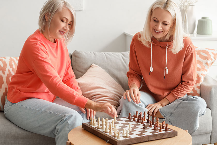 Mature female friends playing chess home Mature female friends playing chess home