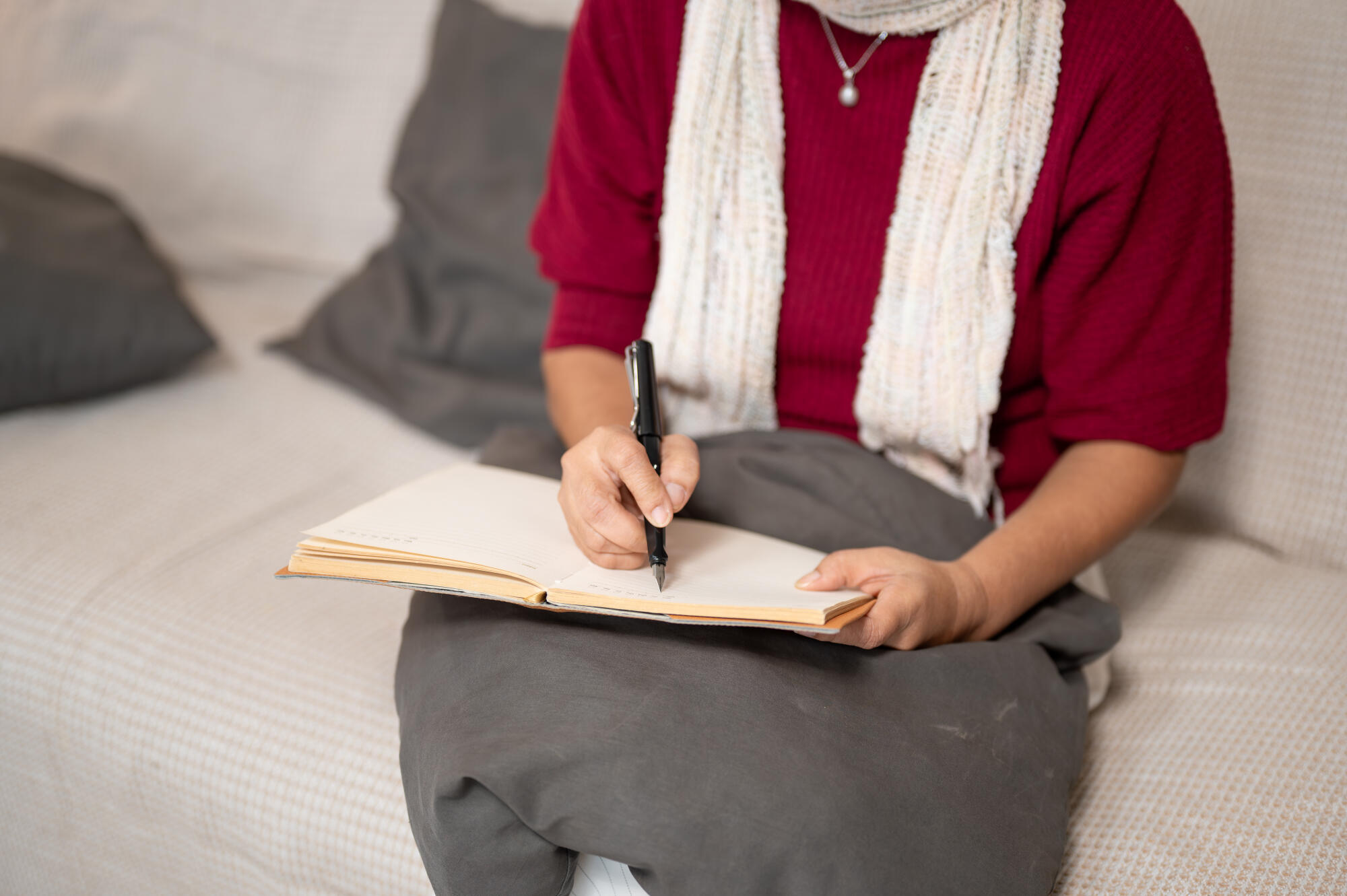 A close up of an Asian retired woman enjoys writing in her diary while sitting on a sofa. A close up of an Asian retired woman enjoys writing in her diary while sitting on a sofa.
