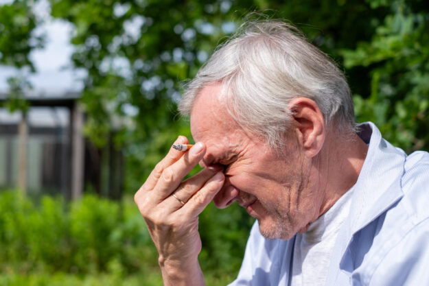 Distressed elderly man with hand on forehead, outdoors. Conveys worry or health issues, suitable for emotive storytelling.