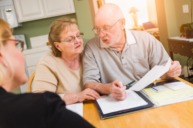 Senior Adult Couple Going Over Documents in Their Home with Agent At Signing.